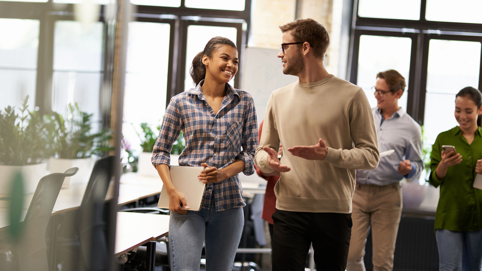 Two Young Diverse Business People, Male And Female Coworkers Talking, Discussing Project And Smiling While Walking Down The Modern Office Two Young Diverse Business People, Male And Female Coworkers Talking, Discussing Project And Smiling While Walking Down The Modern Office